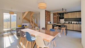 Een moderne keuken met een metselwerk accentmuur, een houten trap en een eethoek met een lange tafel en stoelen.