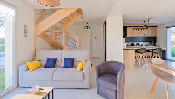 Een moderne woonkamer met een bank, een eettafel en een trap naar een verdieping.