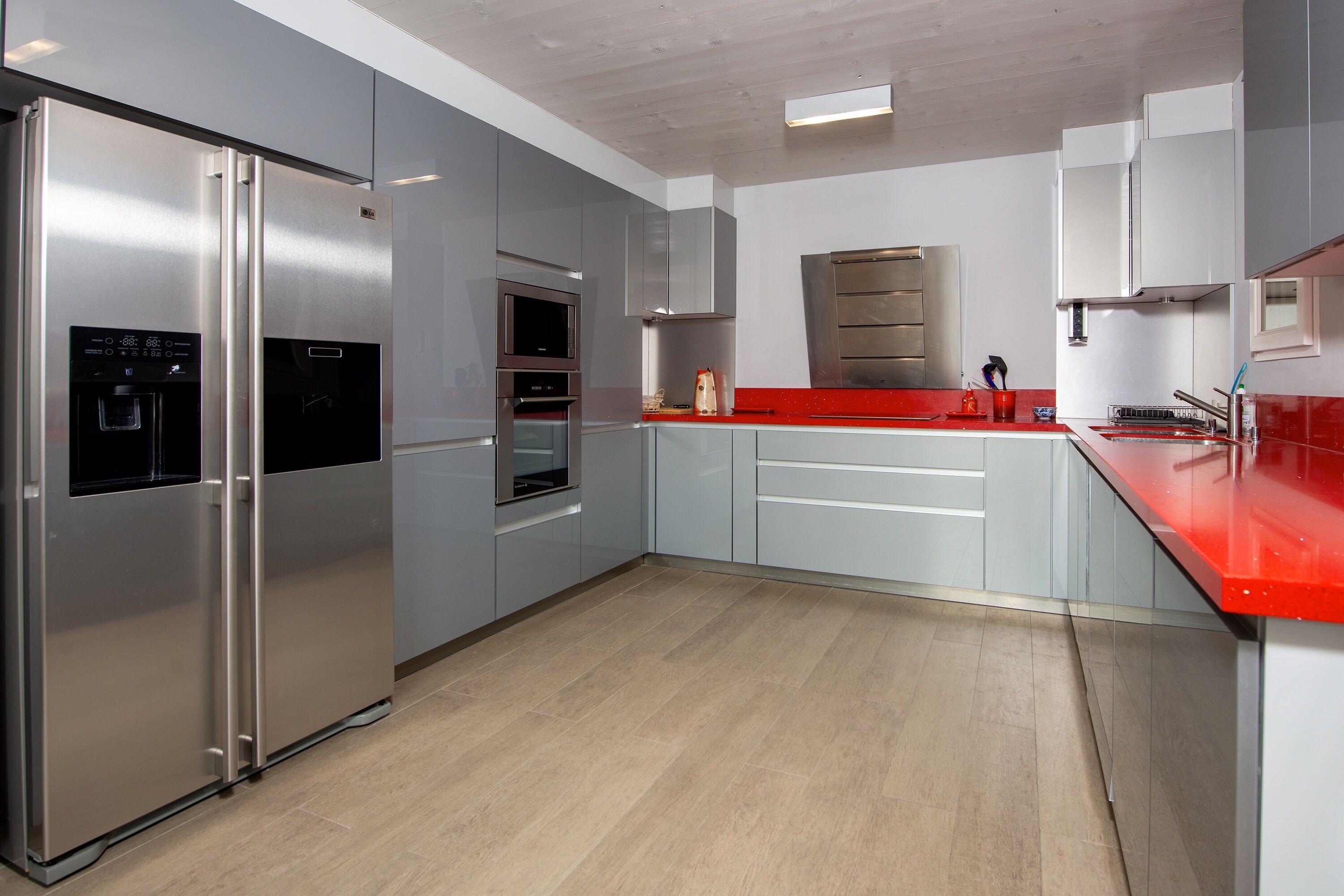 A modern kitchen with stainless steel appliances, a red countertop, and light-colored cabinetry.