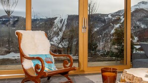 En gyngestol i træ med en hvid pude og en blå pude, et glas med ravfarvet væske og et træbord med en juletræsdekoration.