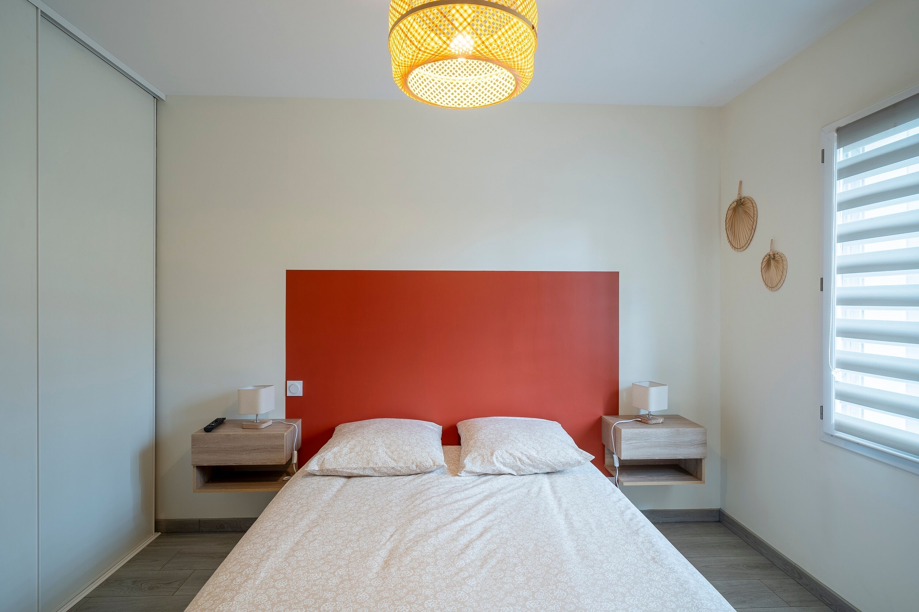 A bedroom with a red headboard, two bedside tables with lamps, a bed with white bedding, and a hanging light fixture.