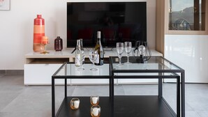 A modern living room with a glass-top coffee table, a flat-screen TV, and a minimalist cabinet. - Stella di Luce - Appt climatisé vue mer (Lumio)