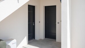 A modern building entrance with two black doors, a small air conditioning unit, and a white wall. - Stella di Luce - Appt climatisé vue mer (Lumio)