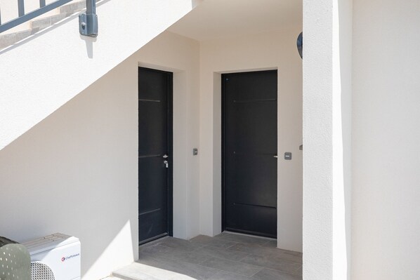 Une entrée moderne avec deux portes noires, un petit appareil de climatisation et un mur blanc.