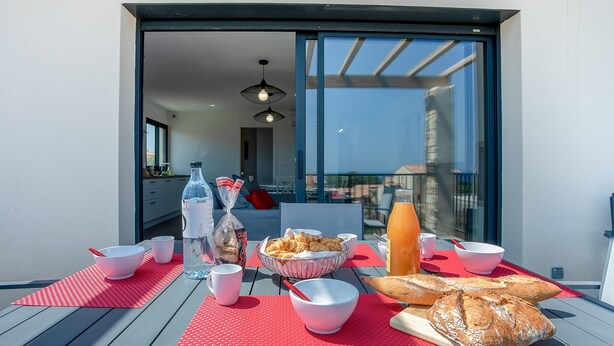 A breakfast setup on an outdoor balcony with a table, bowls, croissants, bread, and a bottle of water. - Stella di Luce - Appt climatisé vue mer (Lumio)