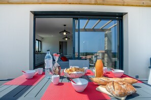 Un plateau de petit-déjeuner installé sur un balcon extérieur, avec une table, des bols, des croissants, du pain et une bouteille d’eau.