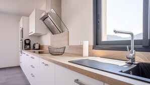 A modern kitchen with a large window, stainless steel appliances, and a wooden countertop. - Stella di Luce - Appt climatisé vue mer (Lumio)