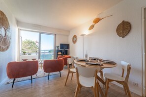 A modern dining area with a round table, white and red chairs, and a view of the outdoors. - La Jetée du Moulleau - Appt 4 personnes vue Bassin (Arcachon)