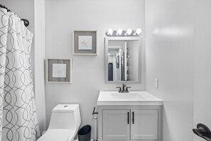 A modern bathroom with a toilet, sink, vanity, and a mirror with lights. - Stone Harbour 304 by Seaside Vacations & Sales (Ocean city)