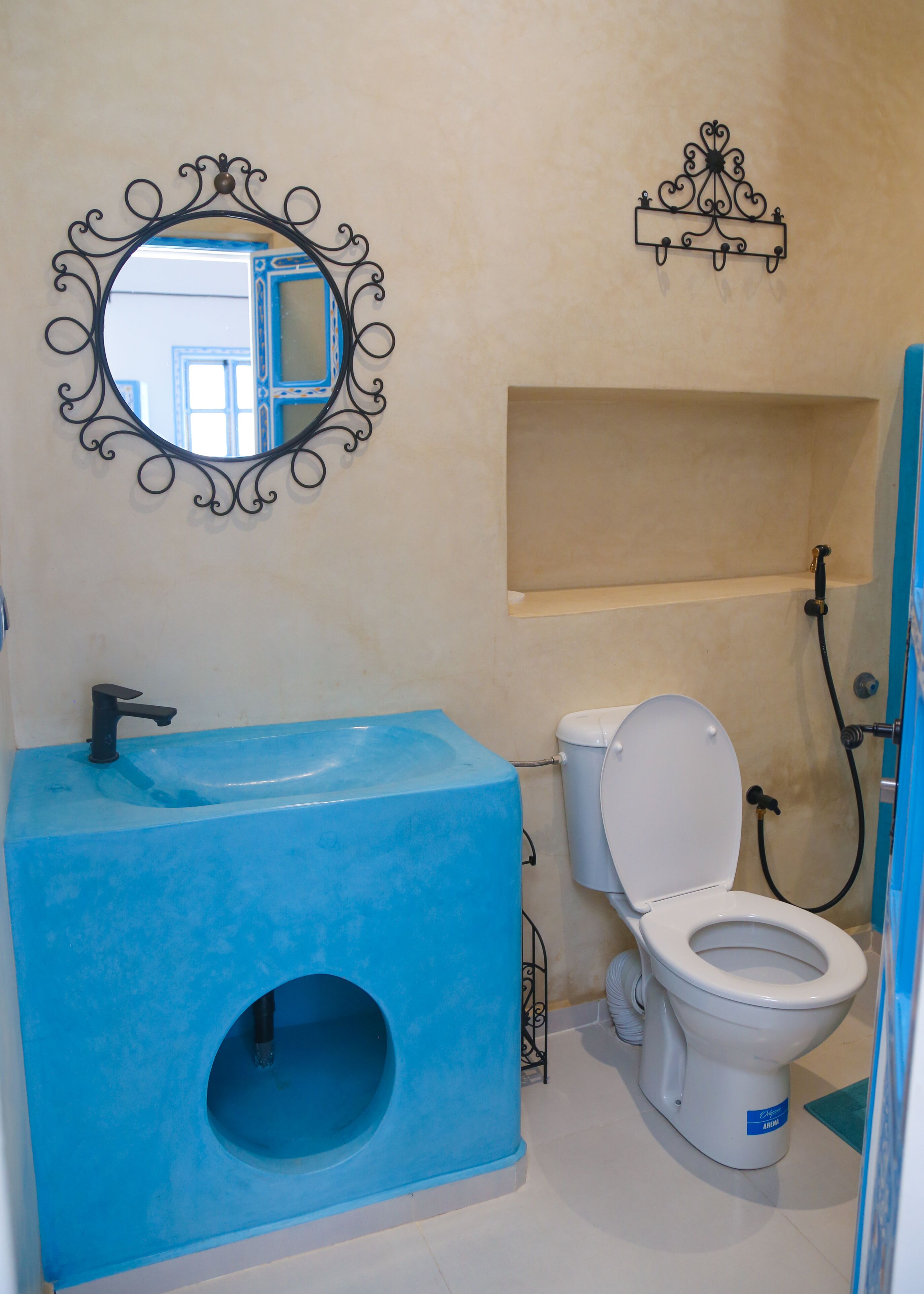 Un baño con un lavabo azul, un inodoro, un espejo con marco decorativo y una zona de ducha.