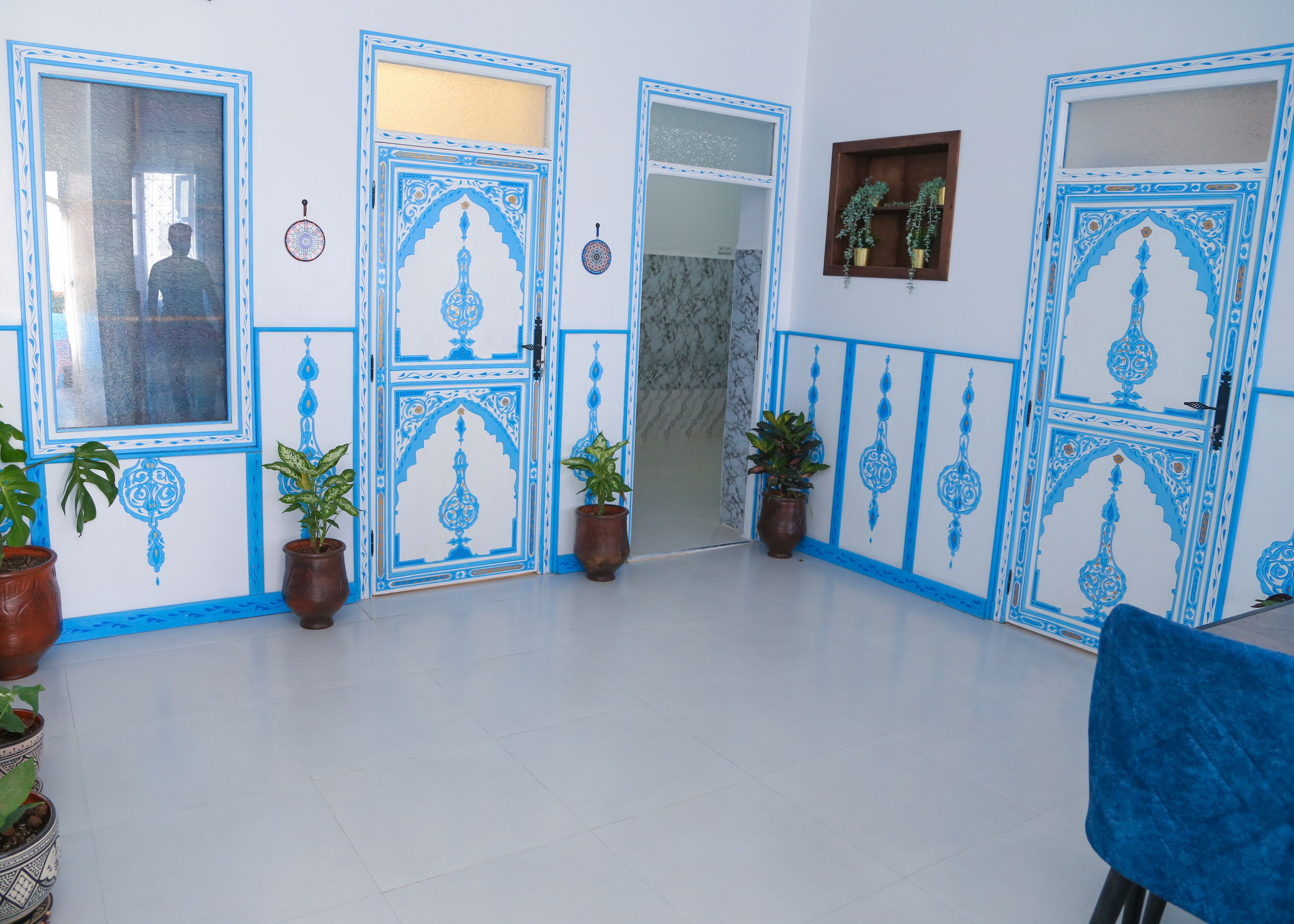 Une pièce avec des portes à motifs bleus et blancs, des plantes en pot et une chaise bleue.