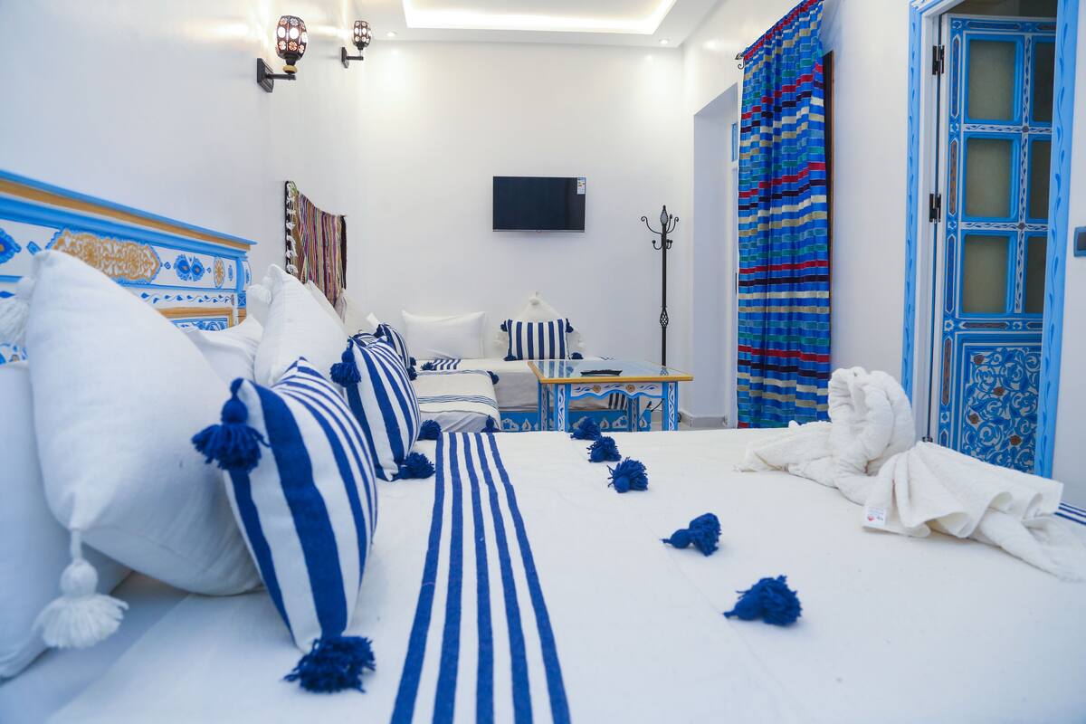 A hotel room with a bed, a television, a nightstand, and a door with a patterned curtain.