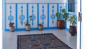 A hallway with a patterned rug, potted plants, a framed picture on the wall, and a door with blue trim.