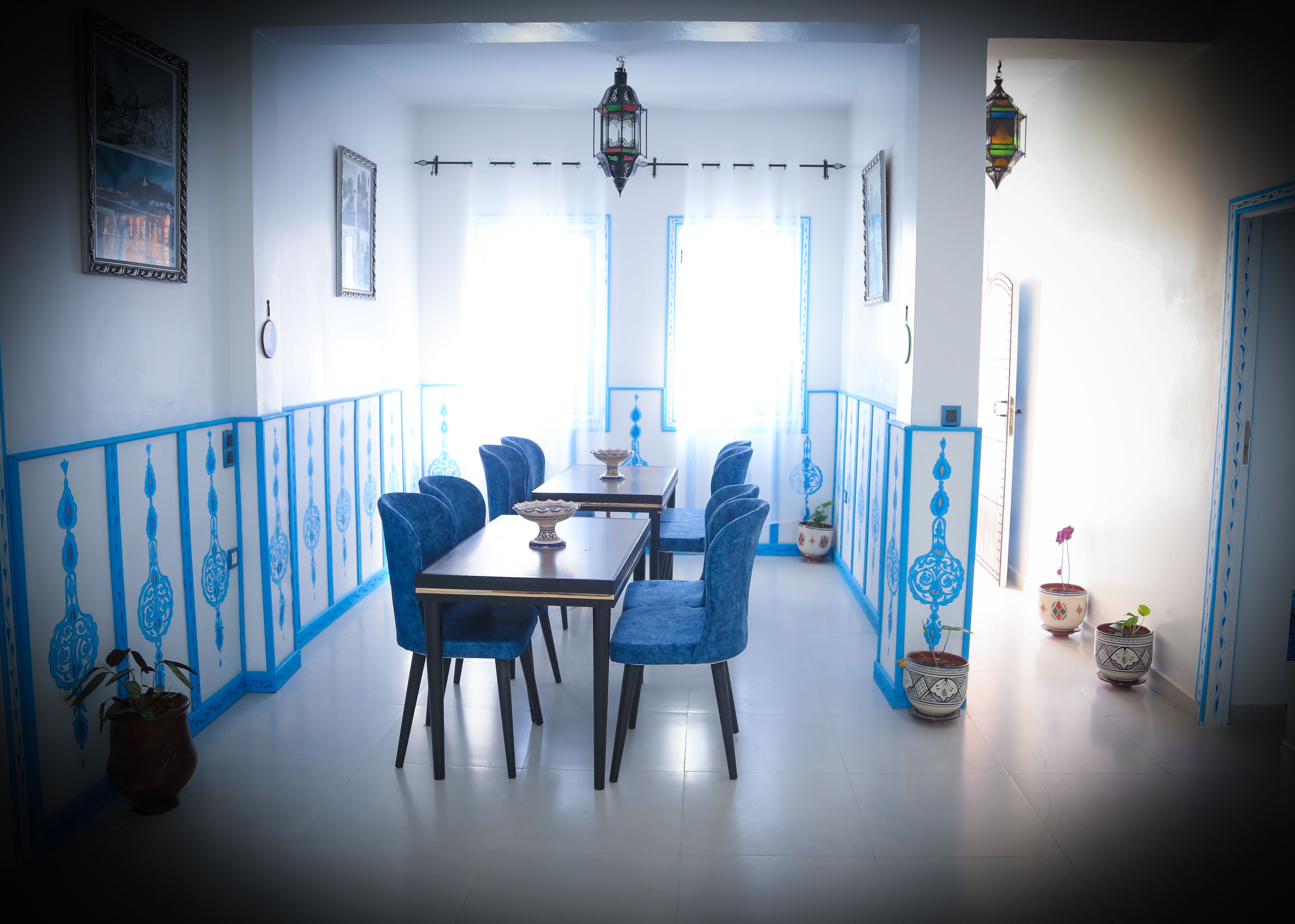 A dining area with a long table and blue chairs, white walls with blue trim, and hanging lanterns.