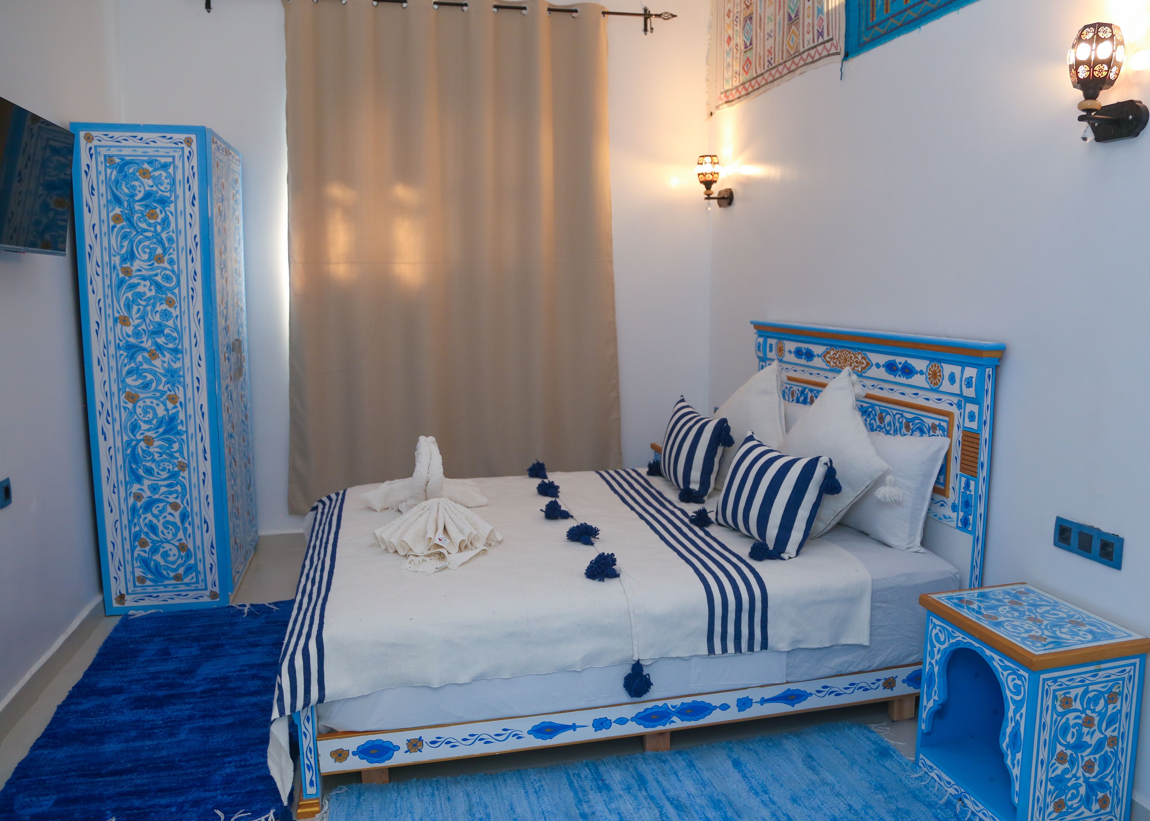 Een net opgemaakt bed met een hoofdbord in blauw en wit dessin, een deken met blauw-witte strepen en decoratieve kussens.