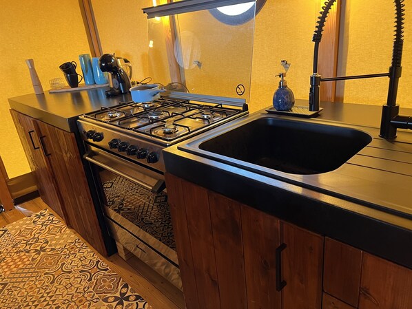 Una cocina con estufa a gas, horno y lavamanos. Hay una cafetera, un hervidor y un dispensador de jabón en la encimera.