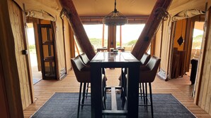 Un espace repas comprenant une table et des chaises en bois, un lustre et de grandes fenêtres donnant sur l’extérieur.