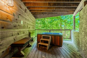 A wooden deck with a hot tub, a bench, and a view of a forest.