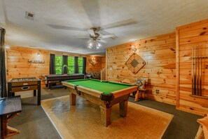 A pool table in a room with wooden walls and a ceiling fan.