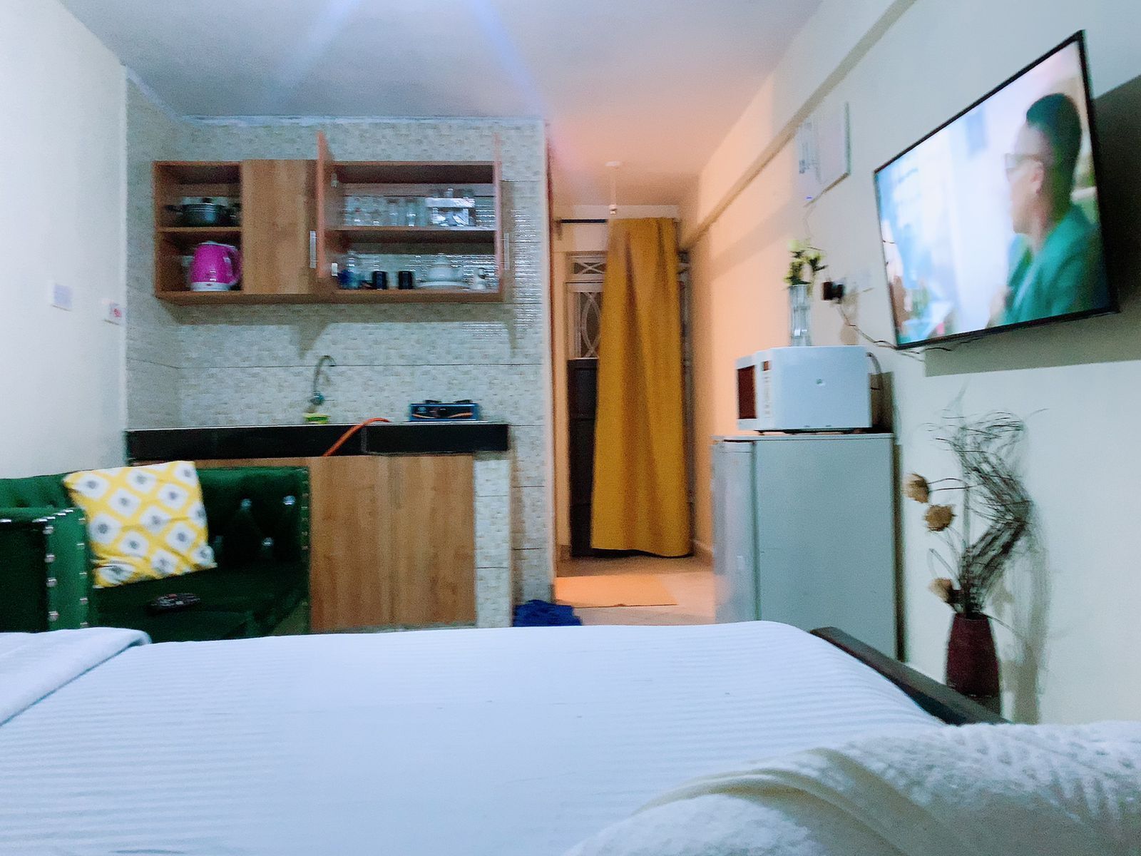 A compact room with a bed, a small kitchenette, a television, and a door leading to another room.