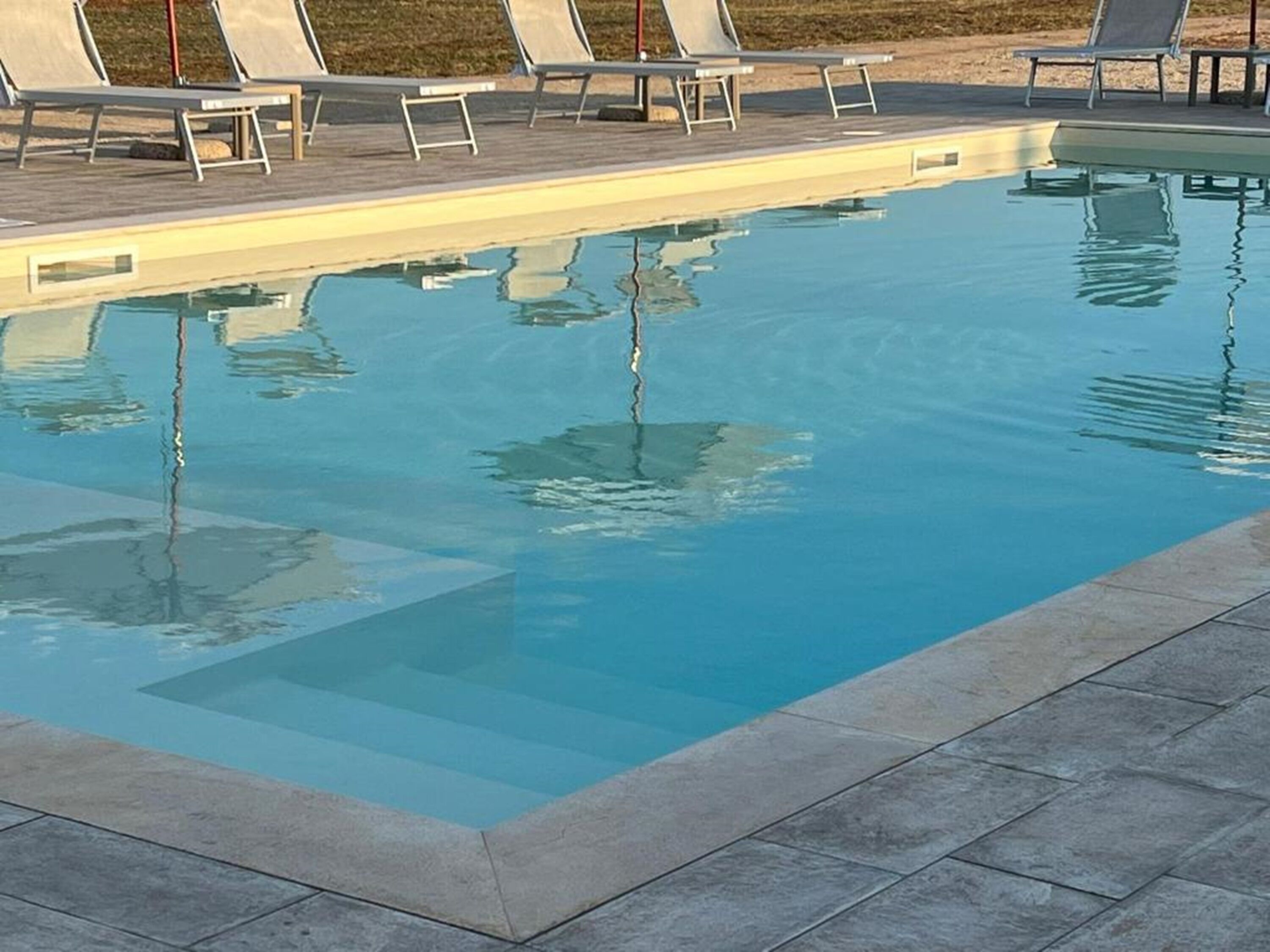 A rectangular swimming pool with clear blue water, surrounded by a tiled deck and several lounge chairs.