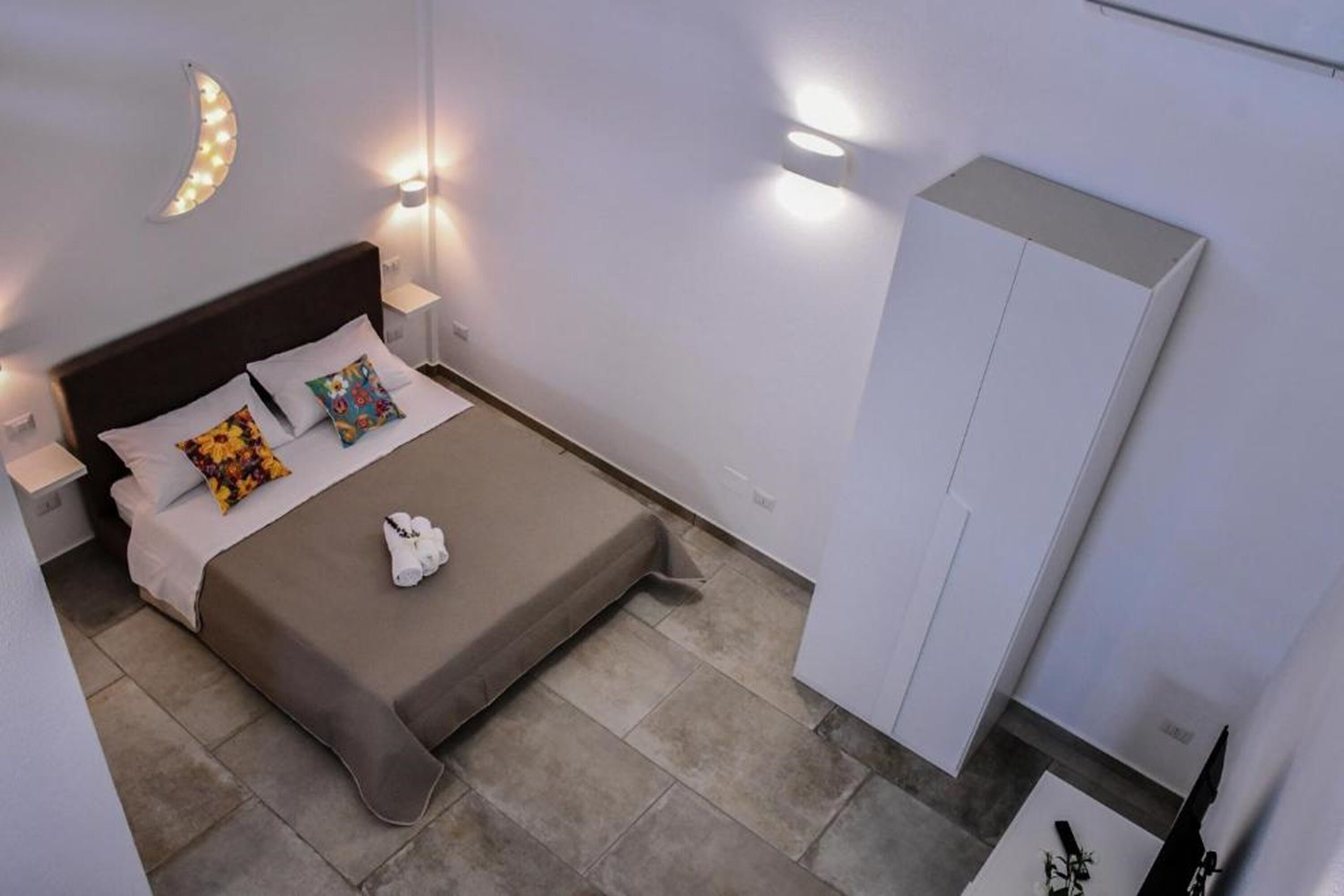 Een keurig opgemaakte slaapkamer met een bed, kussens, een nachtkastje en een garderobe.
