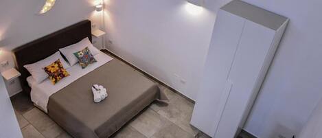 A neatly arranged bedroom with a bed, pillows, a bedside table, and a wardrobe.