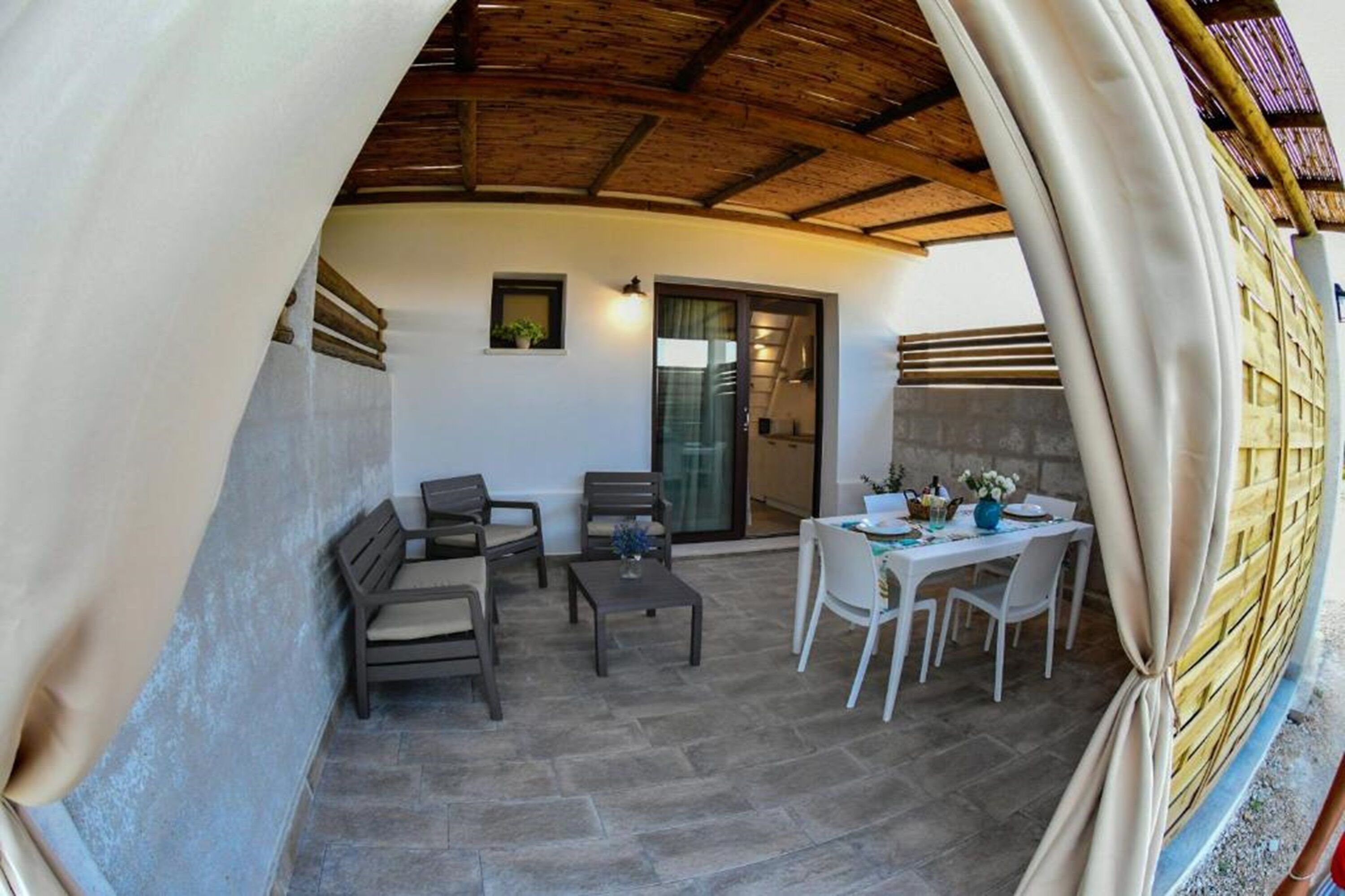 Eine Terrasse im Freien mit Steinboden, Holzboden, einem Esstisch mit Stühlen und einer kleinen Sitzecke mit Sofas.