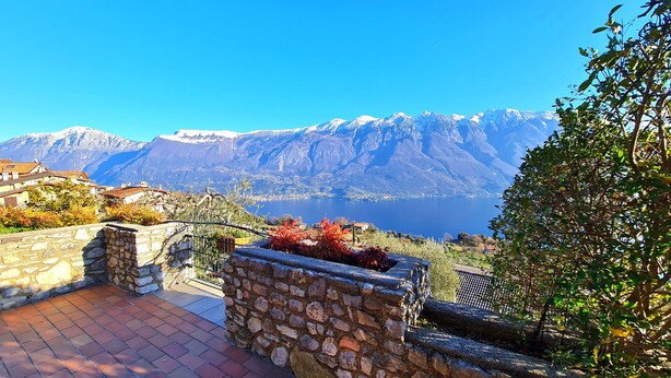A stone pathway leading to a terrace with a view of a lake and snow-capped mountains.