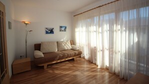 Una sala de estar acogedora con un sofá, una lámpara de pie y un ventanal con cortinas translúcidas.