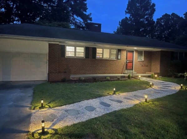A two-story brick house with a garage, a front porch, and a gravel pathway with lights.