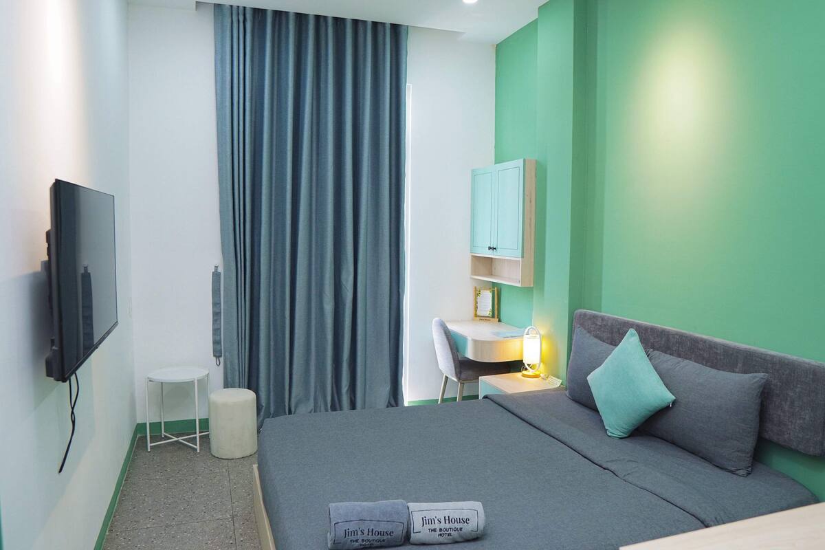 A hotel room with a bed, a desk, a chair, a TV, and a curtain.