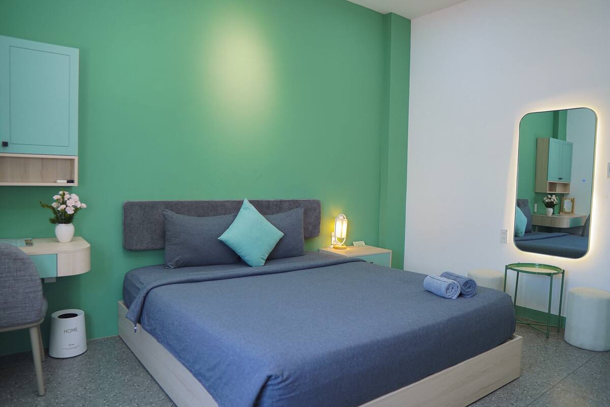 A modern bedroom with a bed, bedside table, lamp, and a mirror.