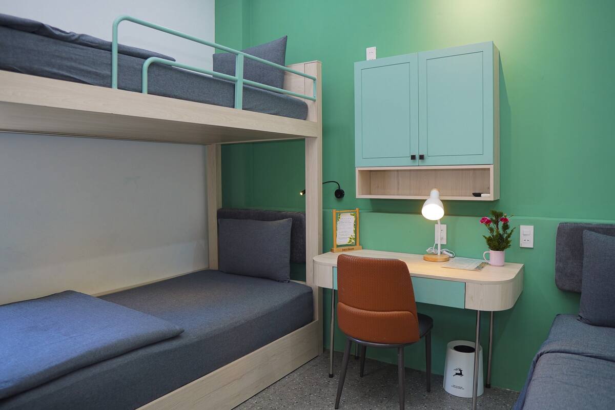 A bunk bed with a desk and chair, a small cabinet, and a trash can.