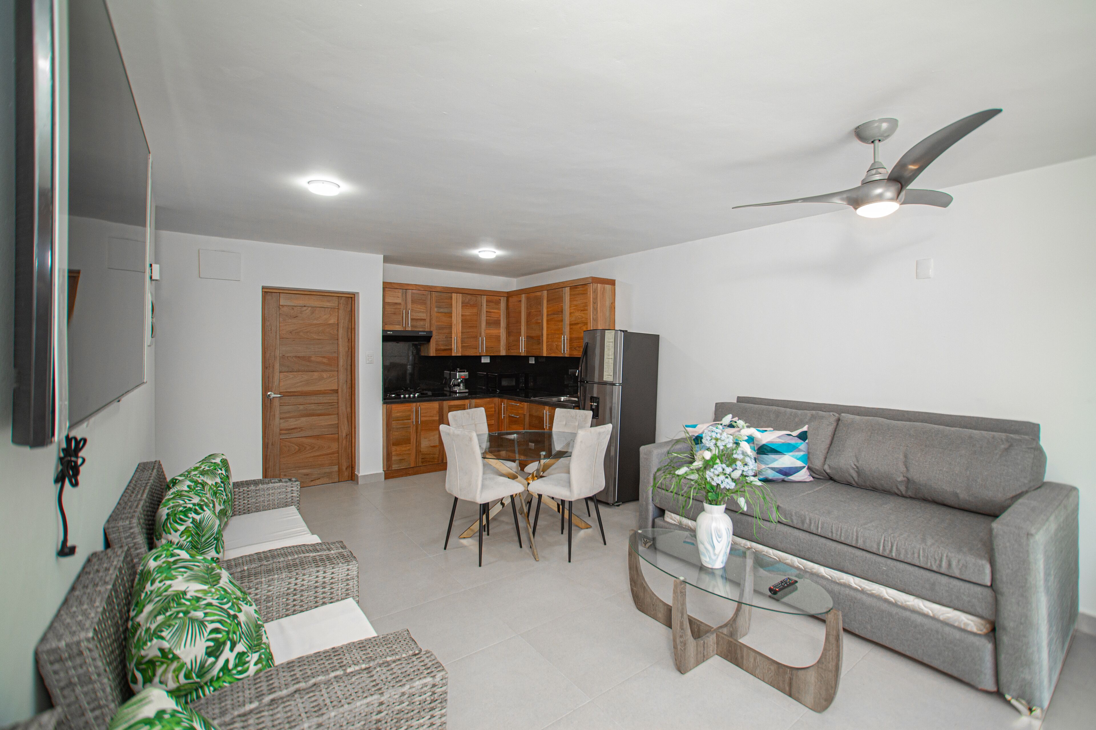 A modern living room with a grey sofa, a glass coffee table, and a dining area with white chairs.