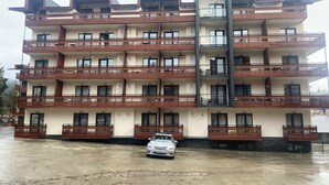 Un edificio de varios pisos con balcones y un coche estacionado adelante.