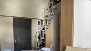 Habitación compacta con mesa de comedor, cuatro sillas, una silla de madera, una escalera con barandillas de metal y un armario.