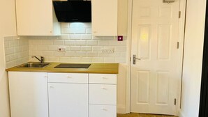 A compact kitchen with white cabinets, a black range hood, a wooden countertop, and a white door. - Newly-built Studio Near Laindon Station (Basildon)