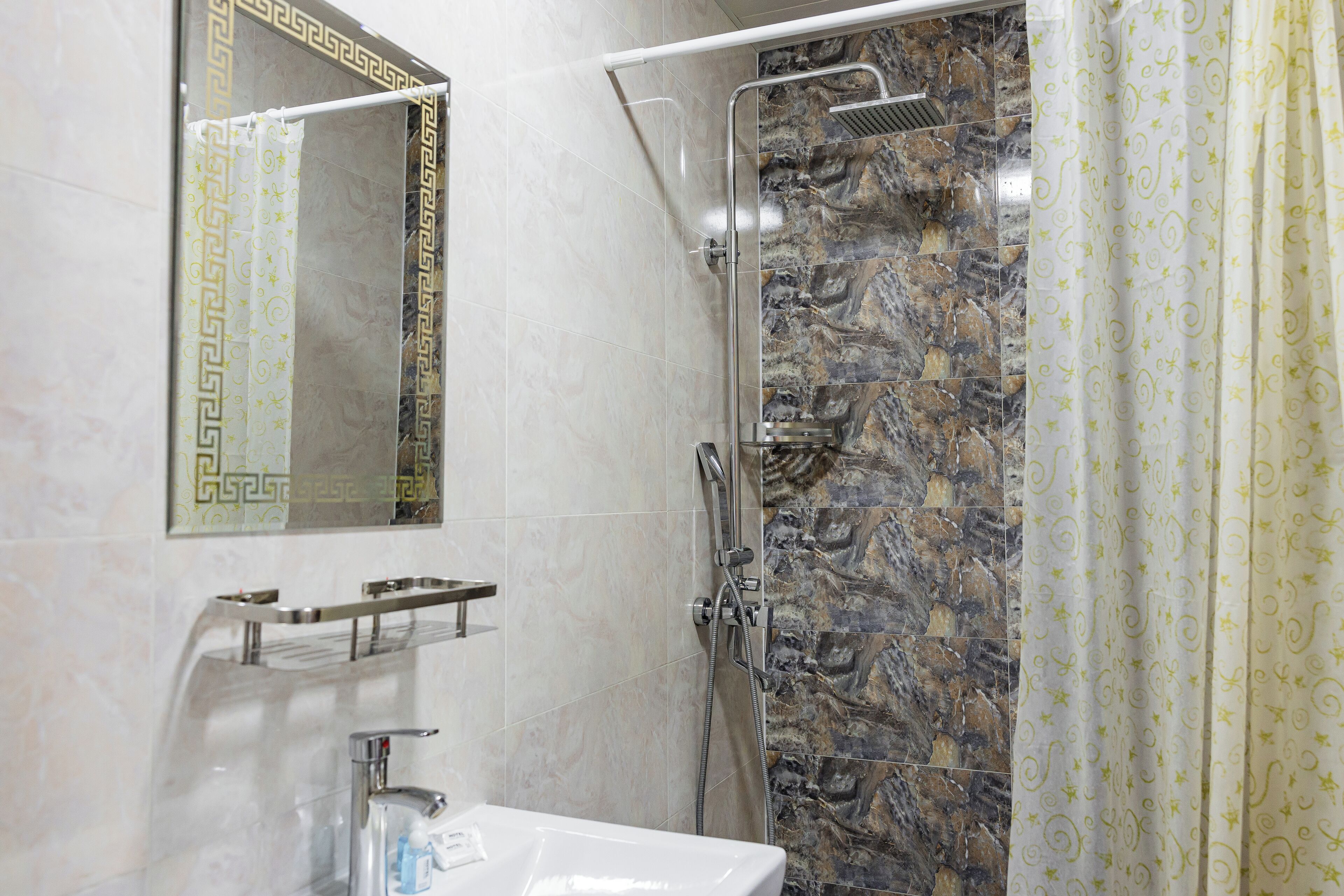 Une salle de bain avec une douche en marbre, un lavabo et un miroir doté d’un cadre décoratif.