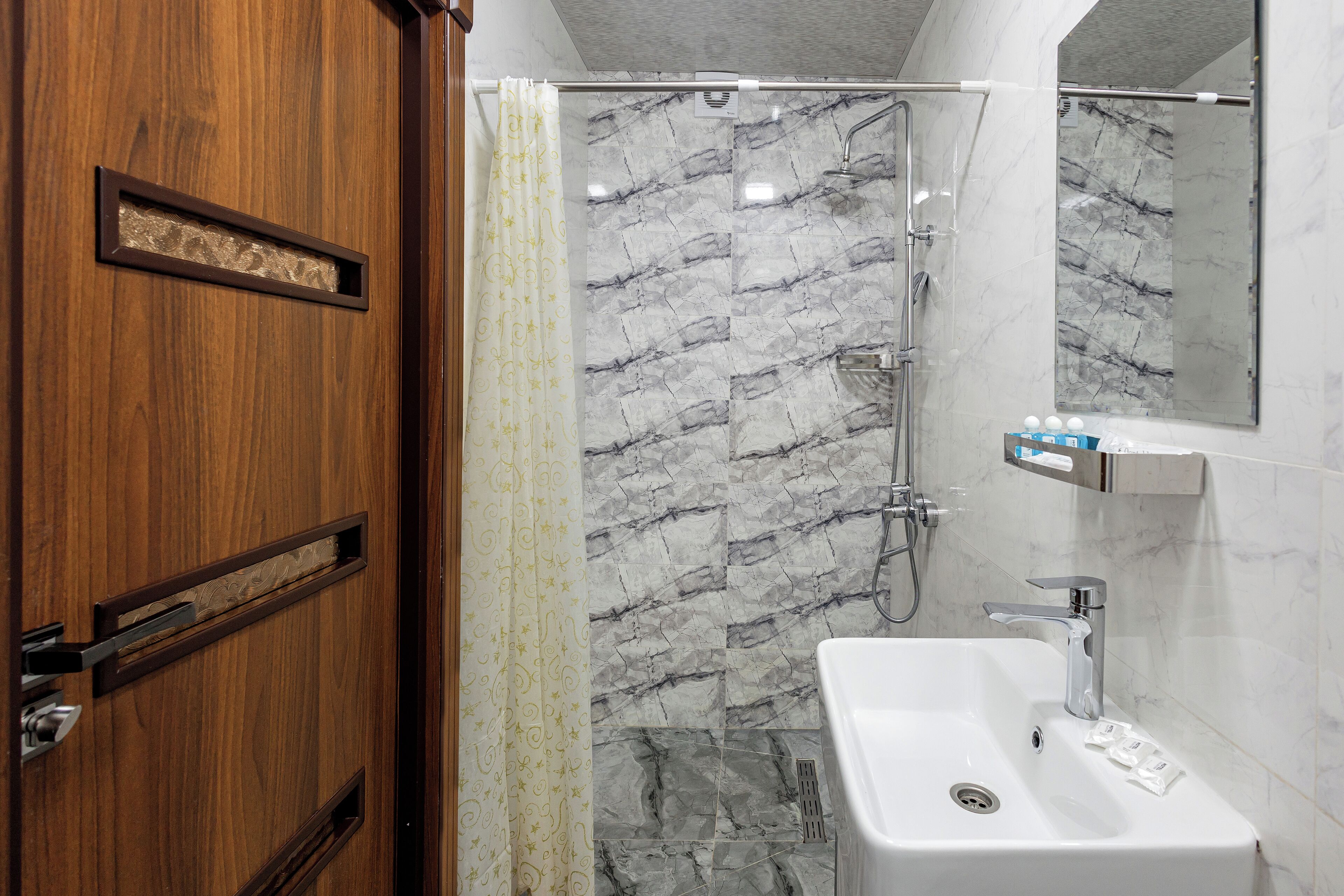 Une salle de bain avec une porte en bois, une douche aux carreaux de marbre et un lavabo blanc avec un miroir au-dessus.