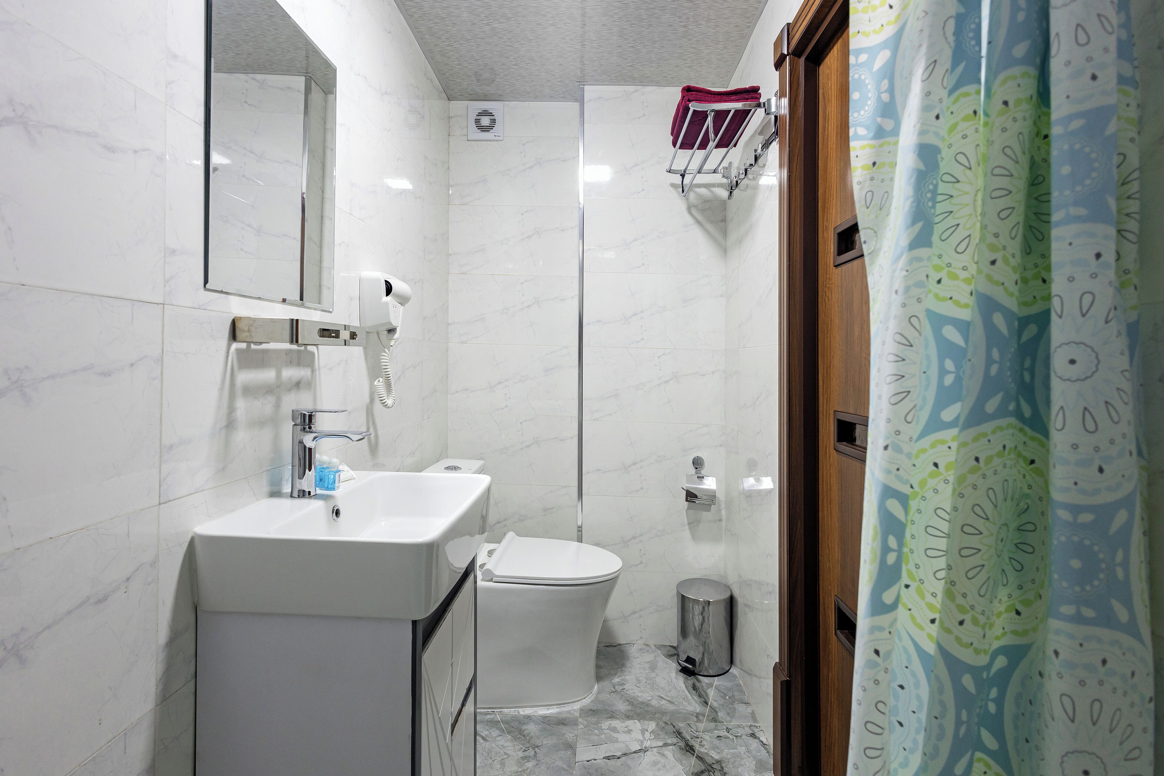 A bathroom with a white sink, mirror, and toilet, a shower, and a patterned curtain.