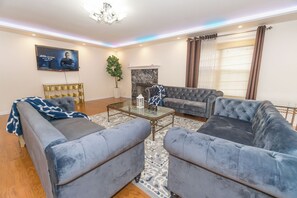 A living room with two grey sofas, a glass coffee table, a TV mounted on the wall, a potted plant, and a fireplace. - Family Haven Retreat, Sleep 14 guests (Carol Stream)