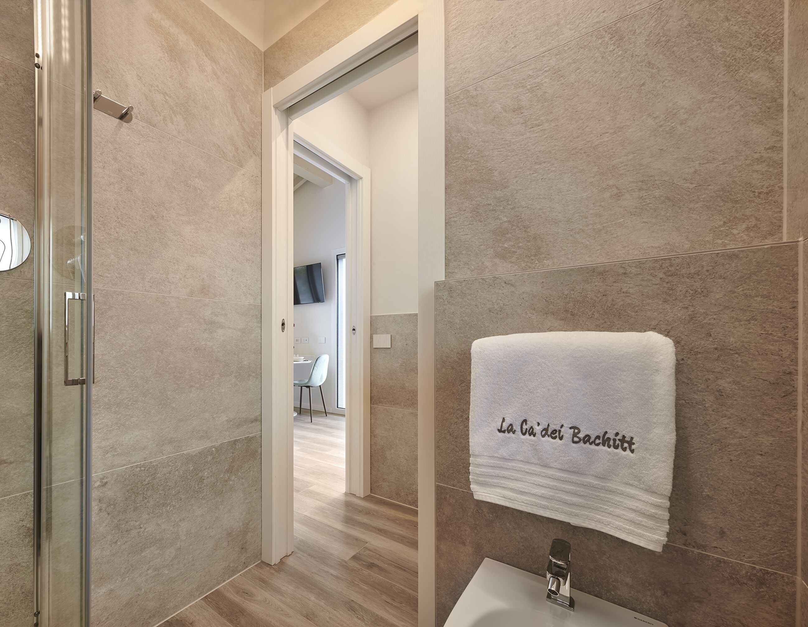 A modern bathroom with a glass shower enclosure, a white sink, and a towel with text on it.