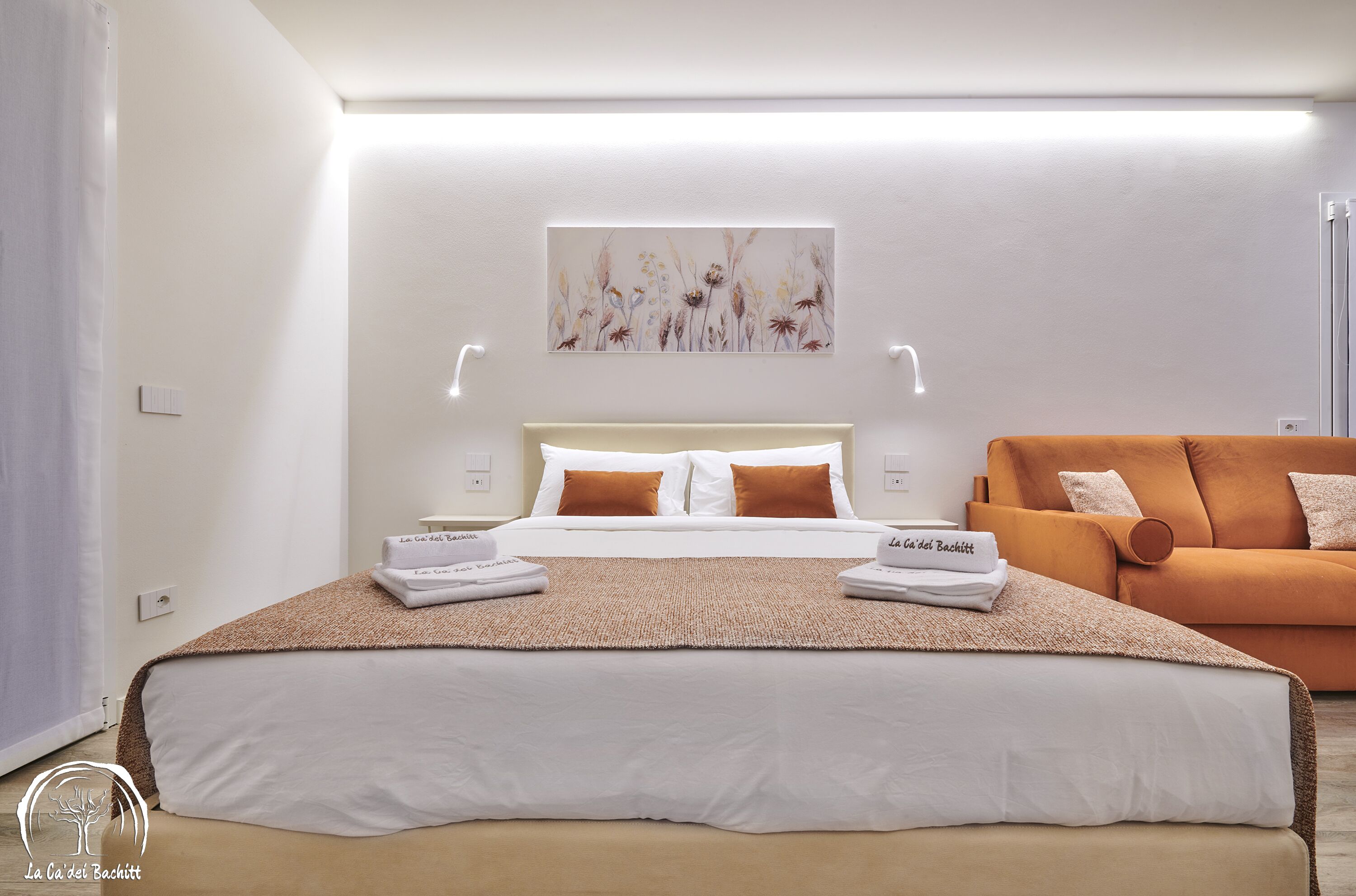 A modern hotel room with a large bed, a sofa, and a wall-mounted artwork.