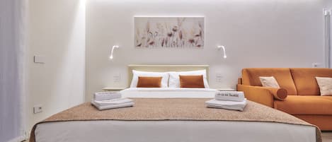 A modern hotel room with a large bed, a sofa, and a wall-mounted artwork.