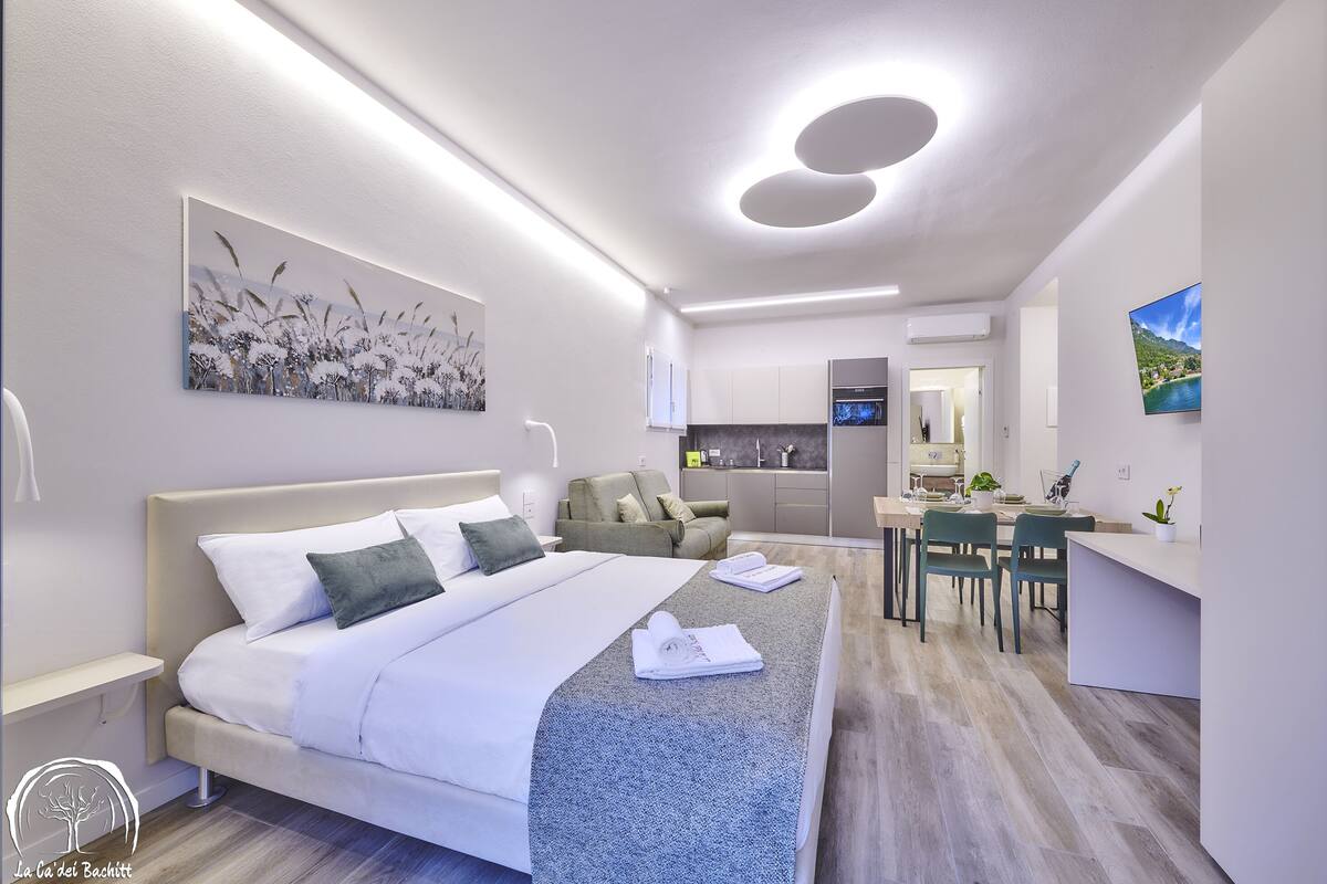 A modern hotel room with a large bed, a desk, and a kitchenette.