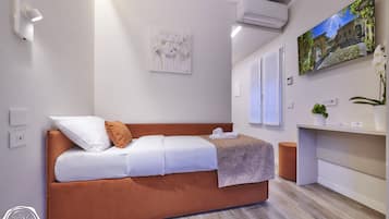 A modern bedroom with a brown sofa bed, white bedding, a wall-mounted air conditioner, a flat-screen TV, and a small potted plant.