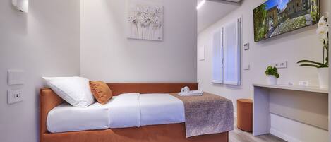 A modern bedroom with a brown sofa bed, white bedding, a wall-mounted air conditioner, a flat-screen TV, and a small potted plant.