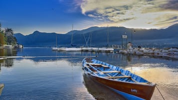 Un lago tranquilo con barcos, un muelle y montañas al fondo.