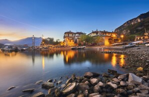 A waterfront property with a rocky shoreline, buildings with balconies, and a mountain backdrop. - Foresteria Ca' dei Bachitt (Lierna)